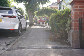 A white electric car parked at the kerb with a cable visible in the pavement which leads to the car charging port