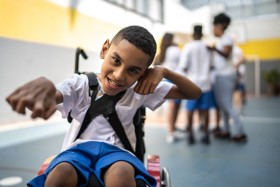 Young person in wheelchair pointing and smiling, looking directly into the camera